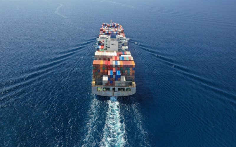 Aerial Drone Ultra Wide Photo Of Huge Container Ship Cruising Deep Blue Open Ocean Sea Near Logistics Container Terminal Port