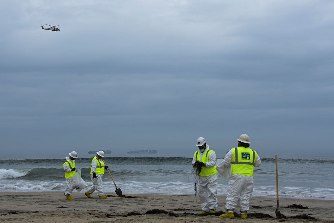 Crews work to clean nearby beaches as containerships anchor offshore.