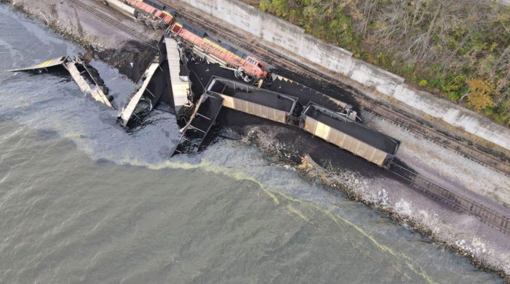 Two locomotives and 10 hopper cars derailed after the train struck the corner of a barge overhanging the rail bed along the Mississippi River.