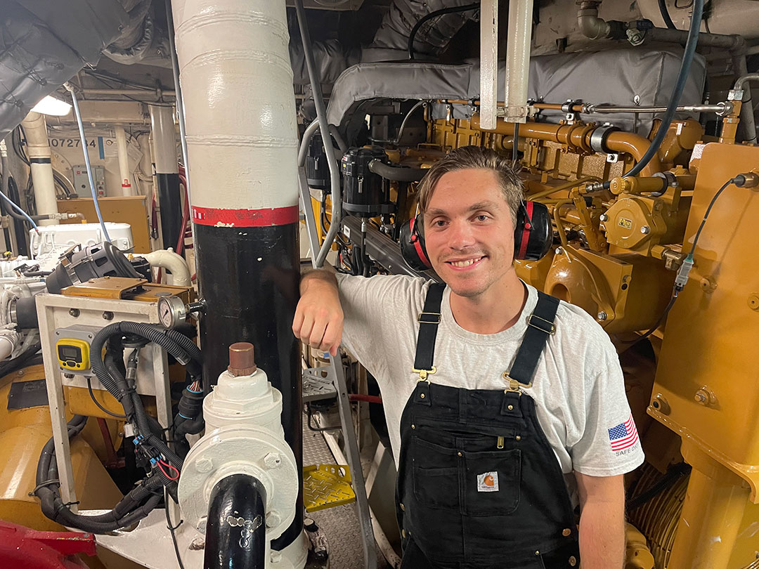 Deck hand-engineer Jackson Lytle standing alongside a Caterpillar 3512 main engine.