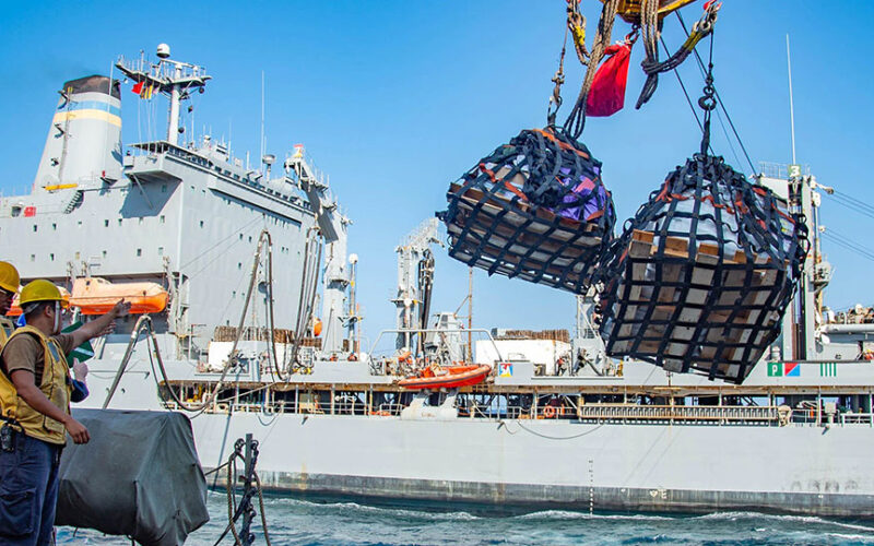 Sealift and Navy crews handle slings of cargo and fuel lines during underway ship-to-ship transfer operations.